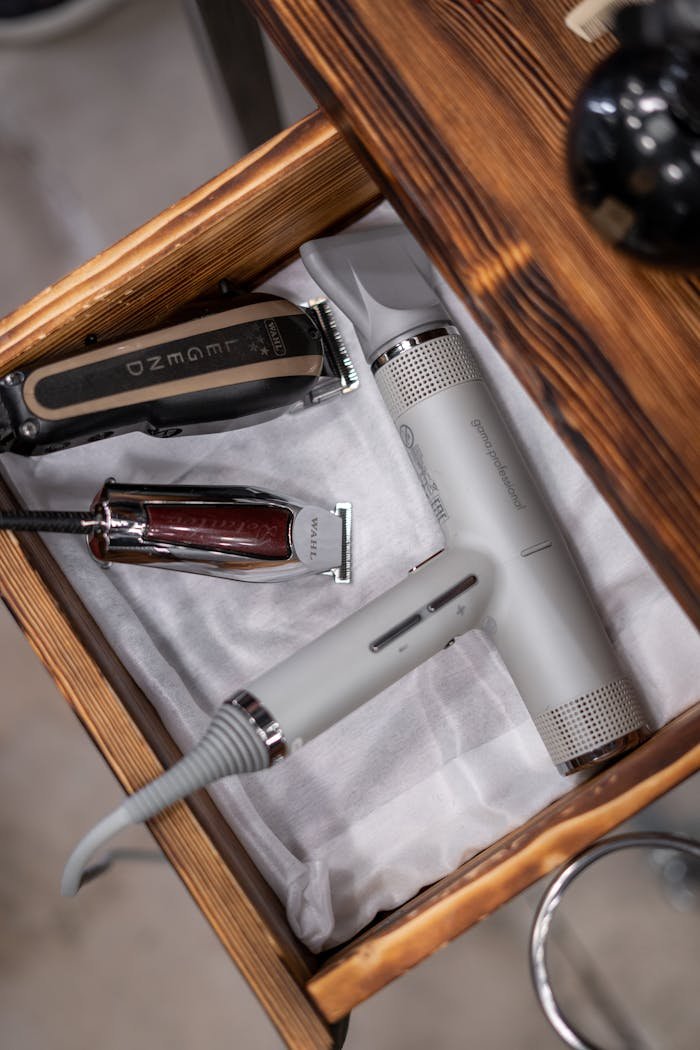 A close-up of barber tools including hair clippers and a hairdryer in a wooden drawer.