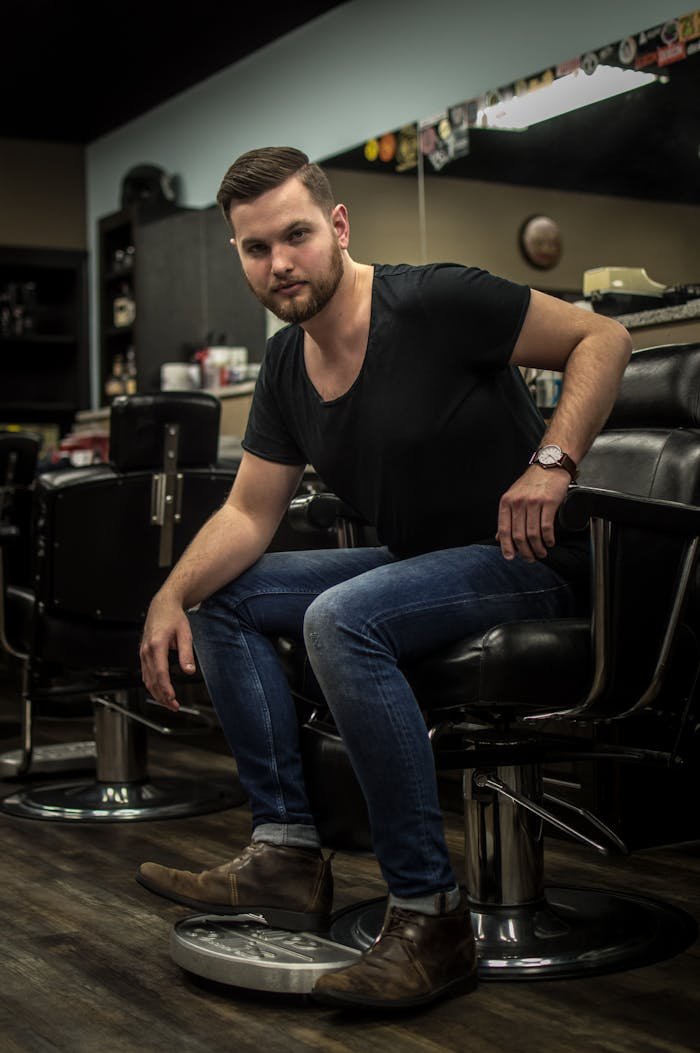 Stylish man sitting in barbershop chair, showcasing casual fashion indoors.